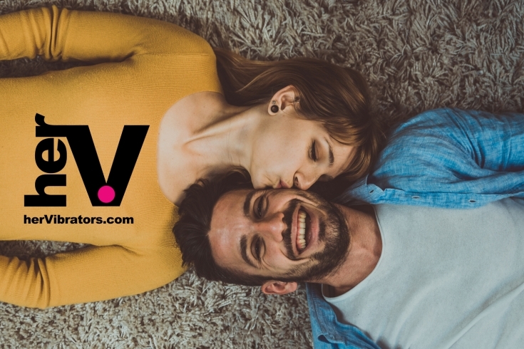 A smiling couple on the floor sharing an intimate moment, representing the Lush Vibrator experience from herVibrators.com