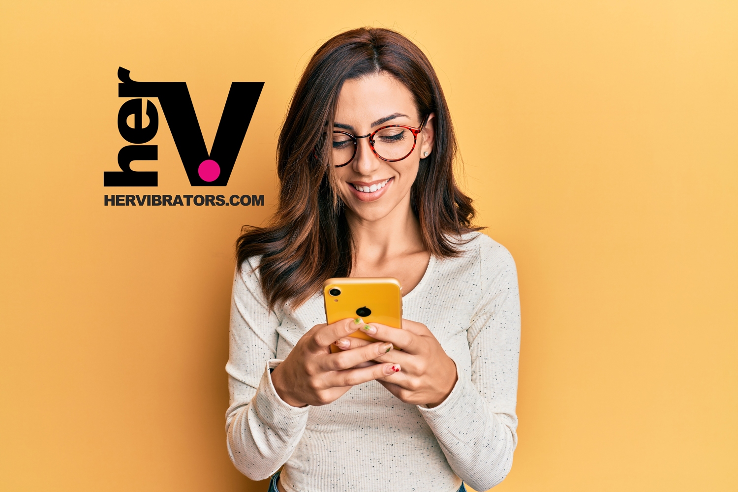 A smiling woman wearing glasses and holding a smartphone against a yellow background, representing the convenience of a remote control bullet vibrator from HerVibrators.com.