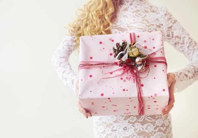 Blonde woman holding floral-wrapped bridal shower gifts while two smiling friends celebrate beside a table of cupcakes and presents.