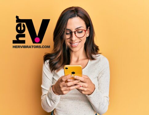 A smiling woman wearing glasses and holding a smartphone against a yellow background, representing the convenience of a remote control bullet vibrator from hervibrators. Com.